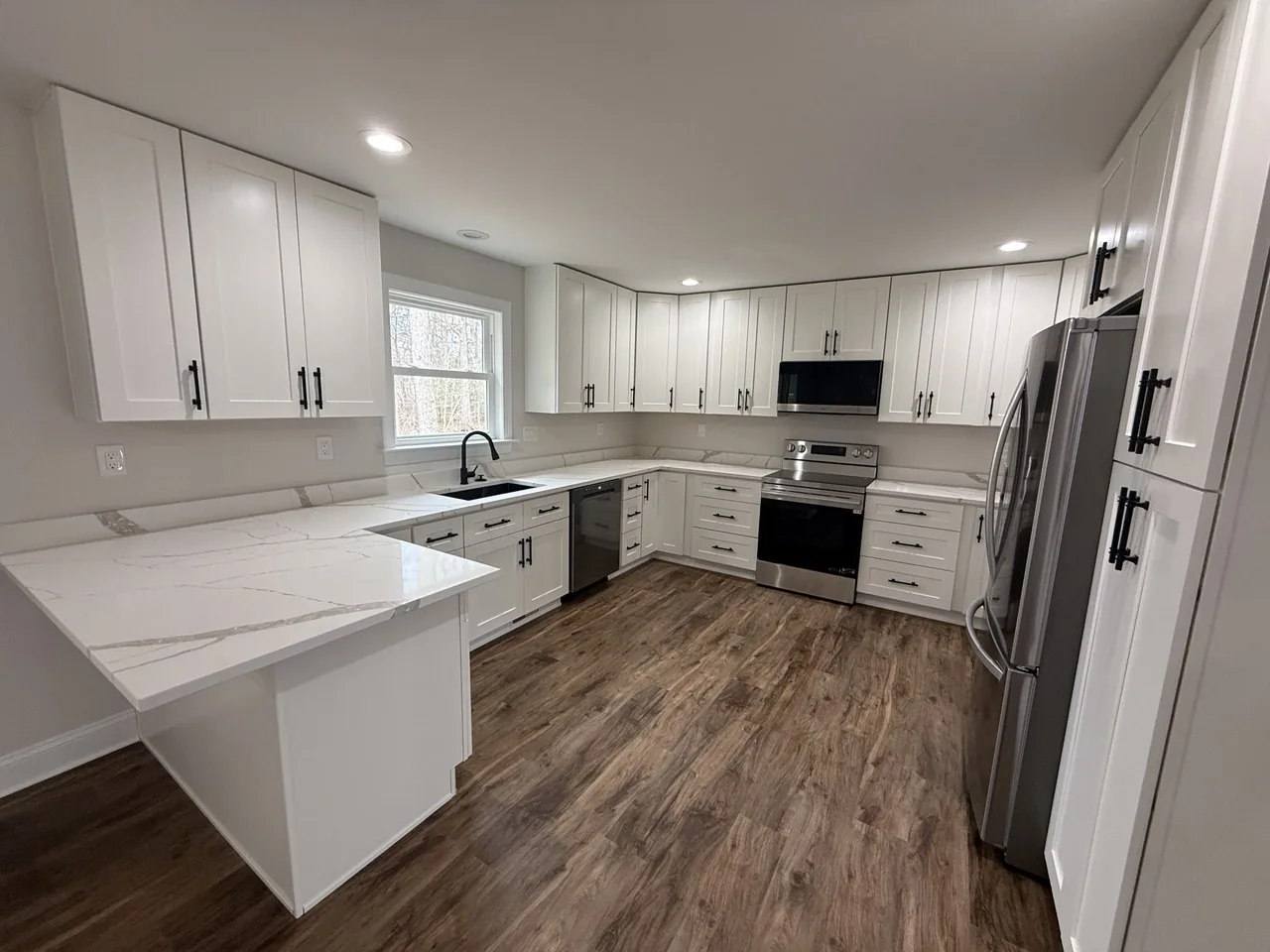 Spacious white kitchen with peninsula and wood flooring